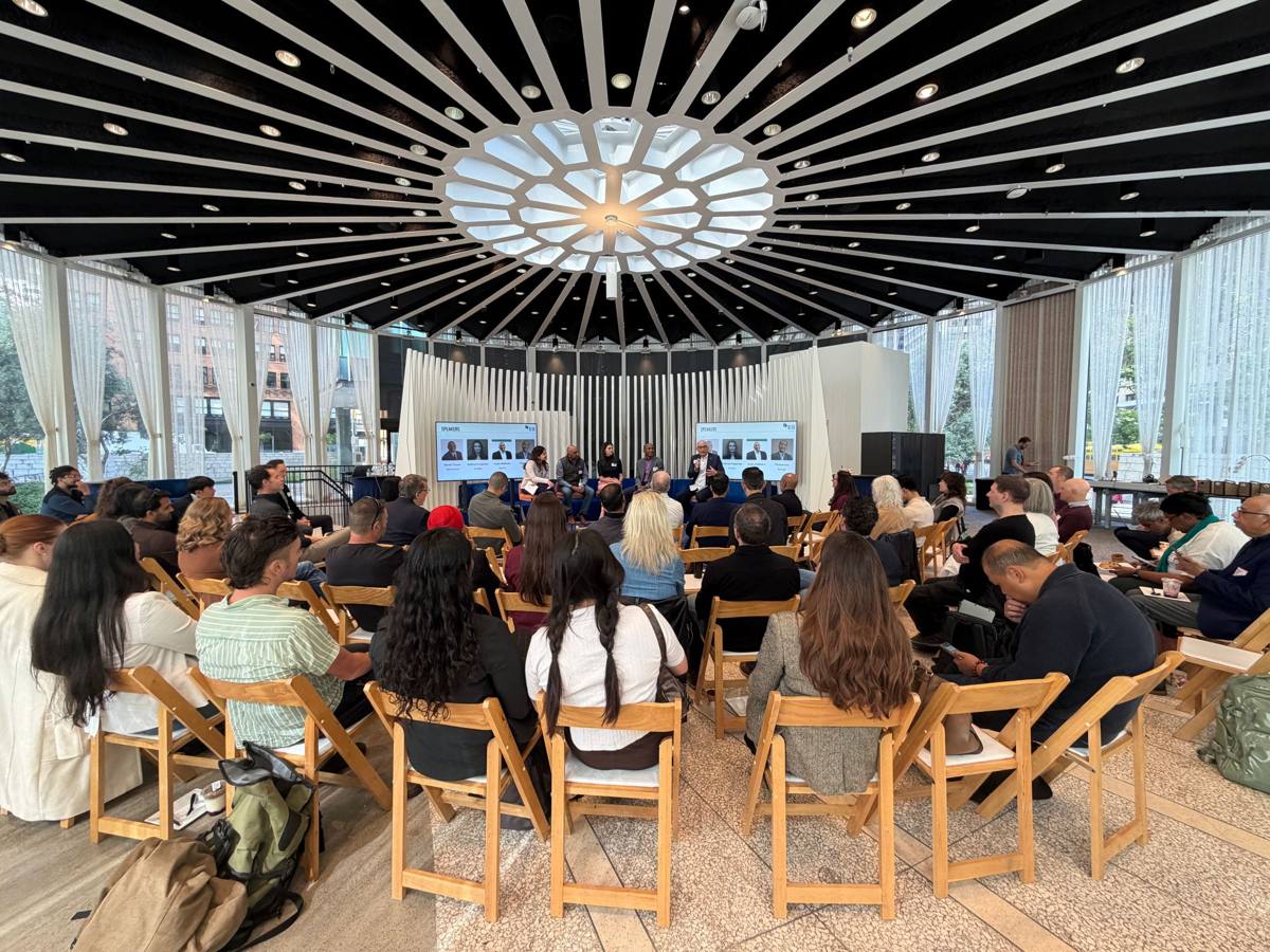 An audience in a round, glass-walled hall listening to a panel discussion.